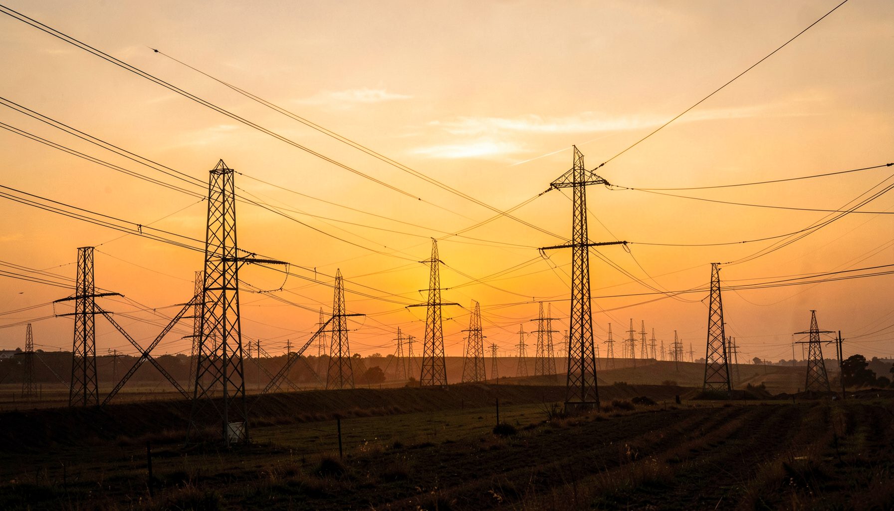 Electrical transmission lines stretching across a warm amber and gold landscape at sunset, evoking power systems and infrastructure