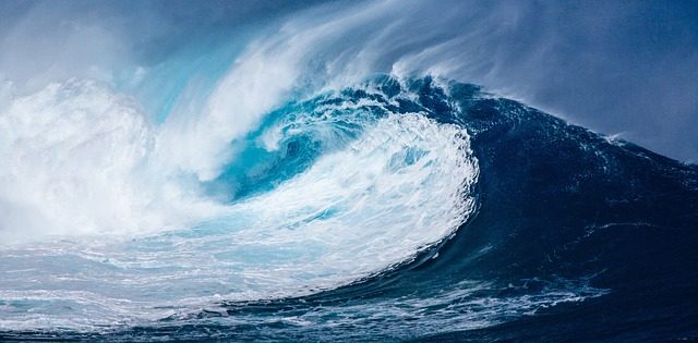 A large ocean wave curling and breaking, with white foam spray and deep blue water, evoking a powerful and dynamic mood