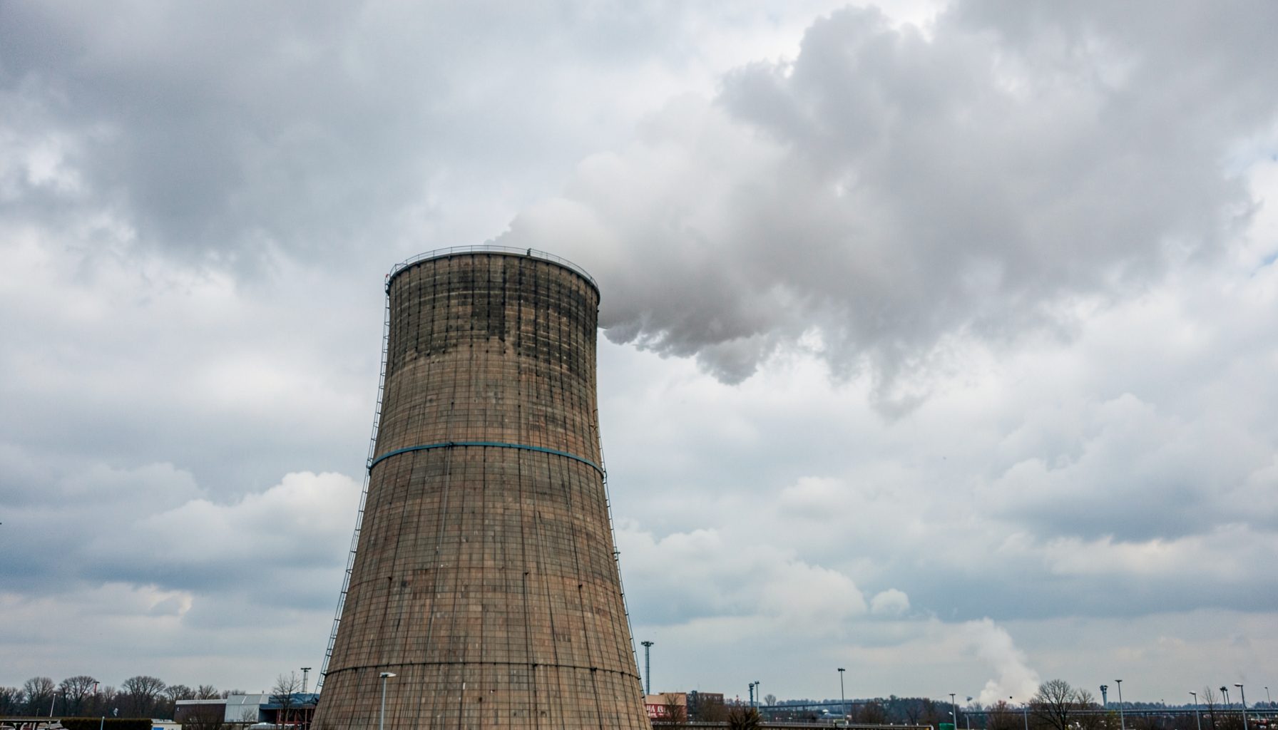 A nuclear power plant cooling tower against a cloudy sky, with steam rising, prompting reflection on the classification of energy sources.