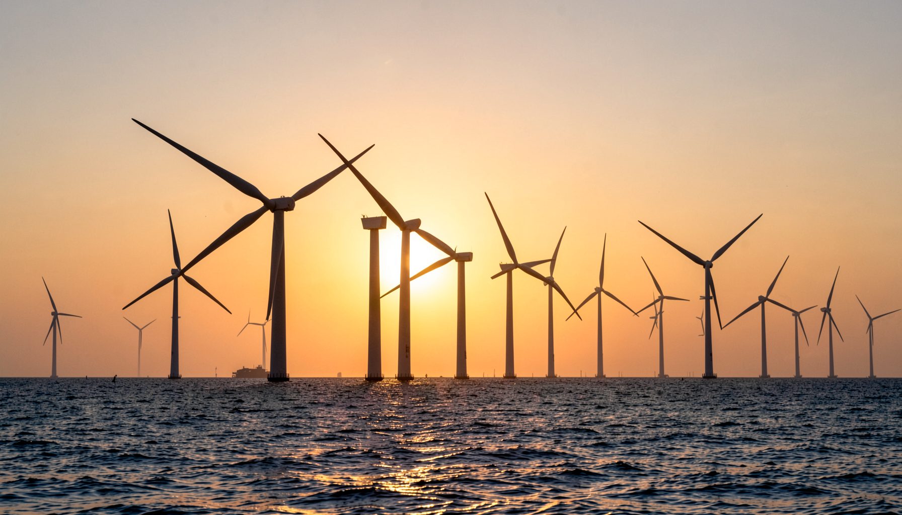 A modern wind farm at sea during golden hour, with turbines silhouetted against a glowing orange and navy sky, conveying clean energy